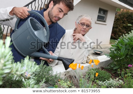 Stok fotoğraf: Young Man Watering Plants With Older Woman