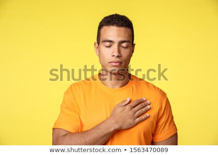 [[stock_photo]]: Peaceful And Hopeful Young Handsome Man Place Hand On Heart Close Eyes And Praying Or Thinking Abou