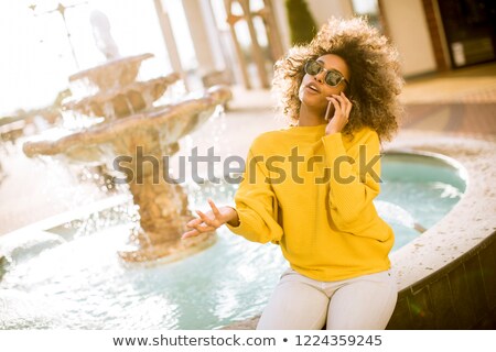 Stock photo: Aftican American Young Woman Sits Near Fountain And Talks On Mob