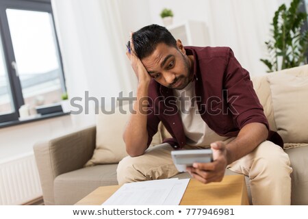 Foto d'archivio: Confused Man With Calculator At Home