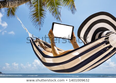 Stok fotoğraf: Woman Lying On Striped Hammock Using Digital Tablet
