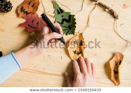 Stock fotó: Hands Of Female With Black Highlighter Drawing Faces On Dry Leaves With Threads