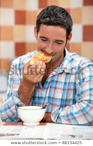 ストックフォト: Smiling Man Eating Croissant For Breakfast With A Magazine