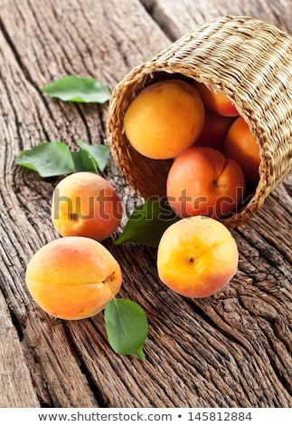 Stock fotó: Fresh Apricots With Leaves In Basket On Wooden Table