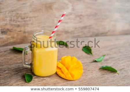 Stok fotoğraf: Juicy Smoothie From Mango In Glass With Striped Red Straw And With A Mint Leaf On Old Wooden Backgro