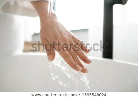 Stockfoto: Hand Of Young Woman Under Pure Warm Water Flowing From Tap Into Bathtub