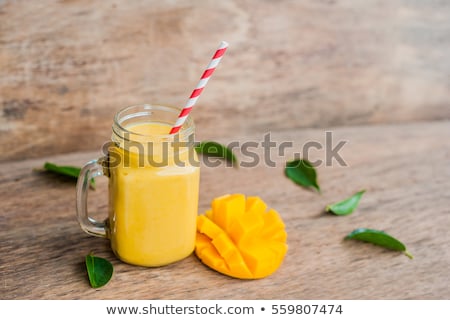 Foto d'archivio: Juicy Smoothie From Mango In Glass With Striped Red Straw And With A Mint Leaf On Old Wooden Backgro