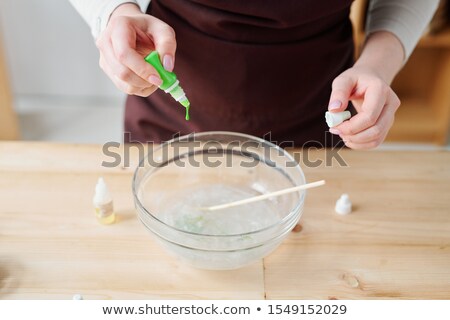 Foto stock: Hands Of Creative Woman Putting Green Color From Bottle Into Liquid Soap Mass