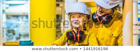 Stockfoto: Young Man And A Little Boy Are Both In A Yellow Work Uniform Glasses And Helmet In An Industrial E