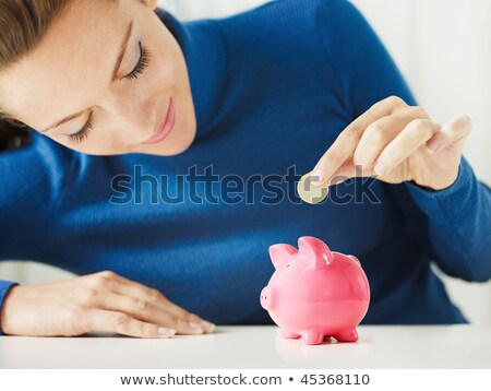 Stock photo: Woman Putting One Euro Coin In Piggy Bank