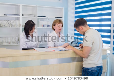 Foto stock: Na · enfermera · sentada · frente · a · una · computadora · en · el · área · de · recepción · de · un · Hospita