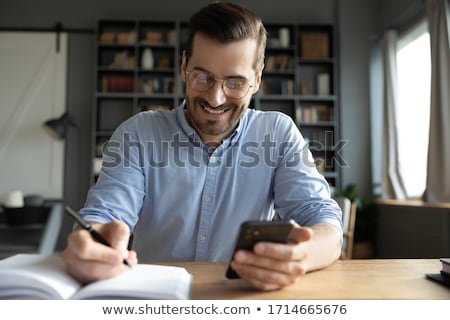 [[stock_photo]]: Businessman Holding Cellphone Writing Schedule In Diary With Pen