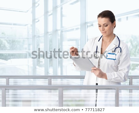Stock photo: Attractive Caucasian Brunette Confident Female Doctor Standing In Office With Binder In Her Hands On