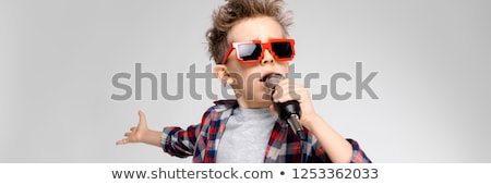 Сток-фото: A Handsome Boy In A Plaid Shirt Gray Shirt And Jeans Stands On A Gray Background A Boy In Red Sung