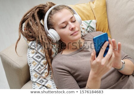 Zdjęcia stock: Pretty Young Restful Woman With Headphones Scrolling In Smartphone On Couch