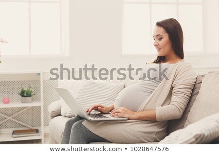 Сток-фото: Smiling Pregnant Young Woman Sitting On Sofa And Using Laptop