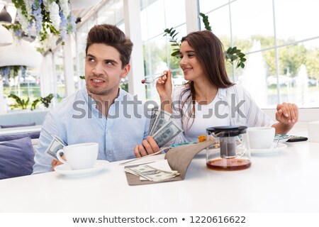 Foto stock: Displeased Confused Loving Couple Sitting In Cafe Holding Check And Money