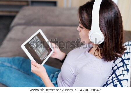 Foto d'archivio: Young Woman In Headphones Looking At Remote Control Panel On Display Of Touchpad