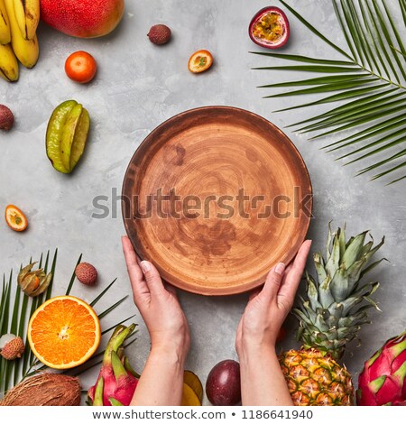 Hands Of A Woman Holding A Brown Empty Plate Around A Different Tropical Fruit Ripe On A Gray Concre Stockfoto © artjazz