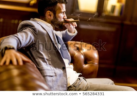 Foto d'archivio: Handsome Man Sitting On A Leather Sofa And Smoking Cigar