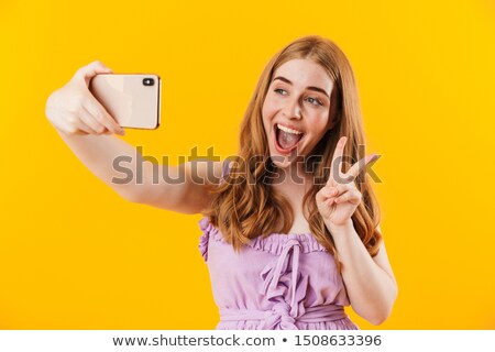 Stockfoto: Emotional Young Women Friends Isolated Over Yellow Wall Background Take A Selfie By Mobile Phone