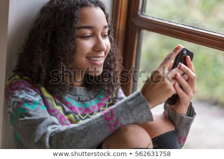 Stockfoto: Curly Hair Teen Girl With Mobile Phone By Window