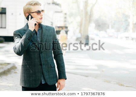 Stockfoto: Photo Of Young Businessman In Suit Talking On Mobile Phone Whil
