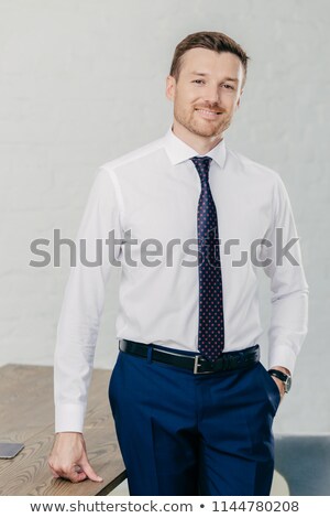 Stock fotó: Vertical Shot Of Handsome Unshaven Cheerful Man Wears Formal Clothes Keeps Hand In Pocket Stand Ne