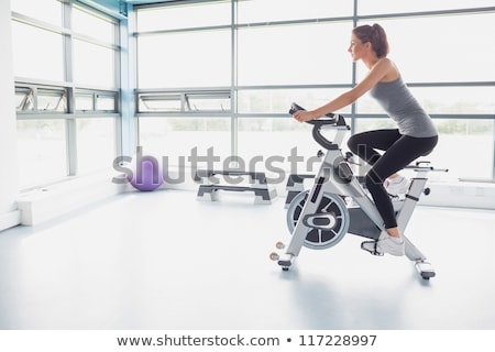 Stok fotoğraf: Smiling Woman Riding An Exercise Bike In Gym