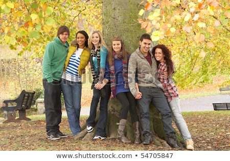 Foto stock: Rupo · de · seis · amigos · adolescentes · apoyado · contra · el · árbol · en · el · parque · de · otoño