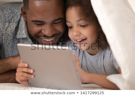 Foto stock: Father And Daughter Using Digital Tablet Under Blanket On Bed
