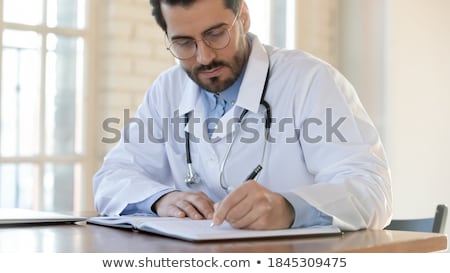Stock photo: Young Male Doctor Writing On A Patients Medical Chart