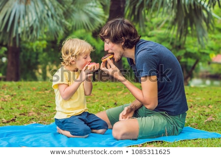 Foto d'archivio: Dad And Son Are Eating A Donut In The Park Harmful Nutrition In The Family