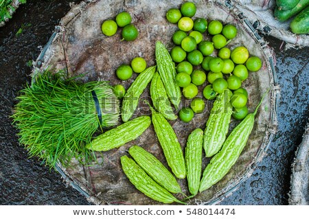 Foto stock: Momordica Chinese Bitter Gourd Or Cucumber Greens And Limesin The Wicker Basket On The Vietnamese