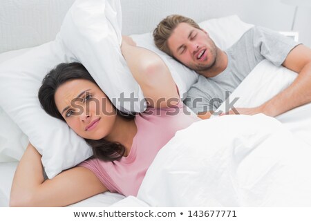 Foto stock: Woman Blocking Ears While Man Snoring On Bed