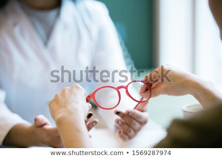 Stockfoto: Pair Of New Eyeglasses In Hands Of Young Optics Clinician During Consultation