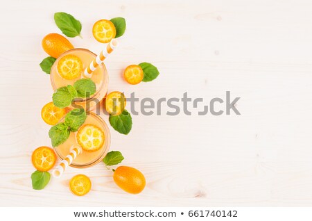 Foto d'archivio: Orange Citrus Kumquat Fruit Smoothie In Glass Jars With Straw Mint Leaf Cute Ripe Berry Top View