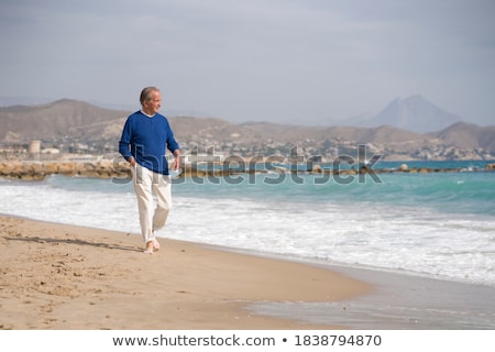 Foto stock: Man With A Surgical Mask In His Hands On The Beach