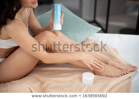 Foto stock: Young Brunette Woman Holding Body Lotion Sitting On The Bed