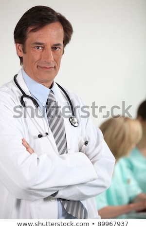 Stockfoto: Male Doctor Stood With Arms Folded Colleagues In Background