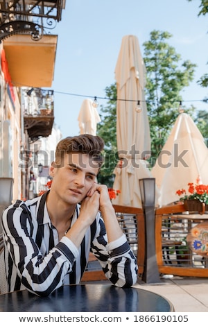 Zdjęcia stock: Happy Young Casual Man Sitting On Chair By Wooden Table And Playing With His Pet