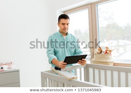 Stock photo: Father With Tablet Pc Assembling Baby Bed At Home