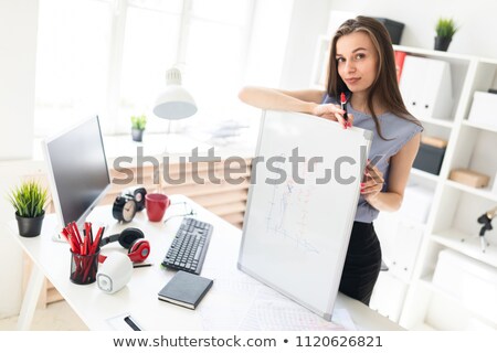 Foto stock: A Young Girl In The Office Is Standing Near The Table Holding A Pencil And A Calculator In Her Hand