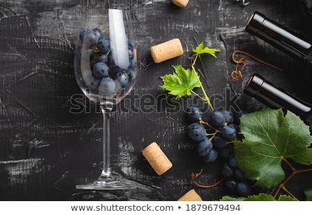 Stock photo: Elegant Glass And Bottle Of Red Wine With Dark Grapes Inside Vintage Wooden Barrel On Black Stone Ba