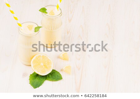 Stock fotó: Yellow Lemon Smoothie In Glass Jars With Straw Mint Leaf Cut Lemon Top View White Wooden Board B