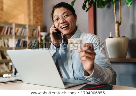 Stok fotoğraf: Pleased Asian Male Student In Eyeglasses Talking By The Smartphone