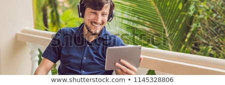 Stockfoto: Man In Tropics Talking With Friends And Family On Video Call Using A Tablet And Wireless Headphones