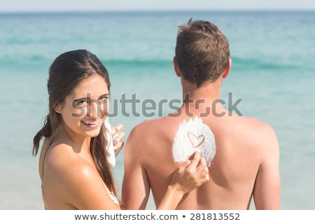 Stockfoto: Cheerful Young Man Applying Sunscreen Cream On A Beach