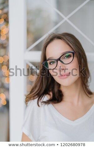 Stockfoto: Vertical Shot Of Charming Woman In Optical Glasses Dressed Casually Poses Indoor Against Christams