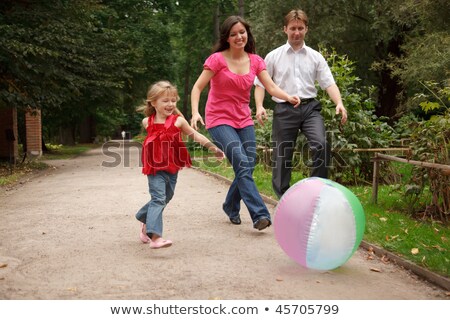 Сток-фото: Little Girl In Jeans And Red Dress Plays With Big Inflatable Ball In Park Together With Parents